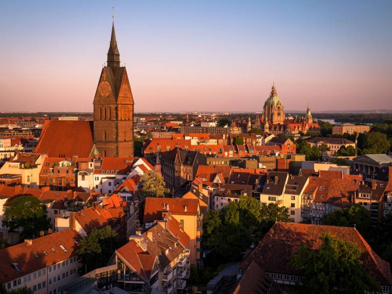 Stadtansicht im Abendlicht mit der gotischen Marktkirche und demprächtigen Neuen Rathau mit grüner Kuppel zwischen roten Dächern.